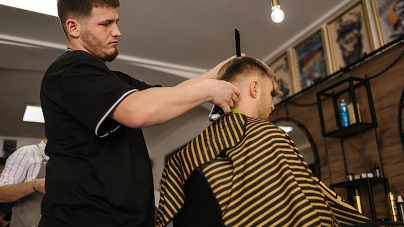 Back view of barber using trimmer to make haircut for customer