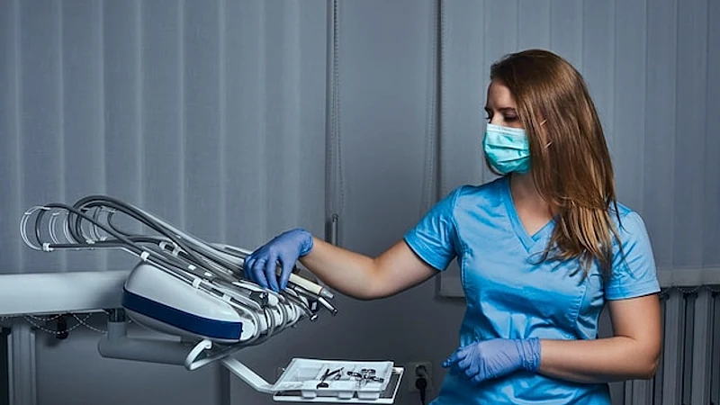 Female dentist wearing a uniform and mask sitting on a chair at his workplace in a dental clinic.