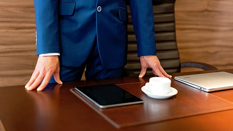 Professional businessman in blue suit standing by a desk with a tablet and coffee cup.