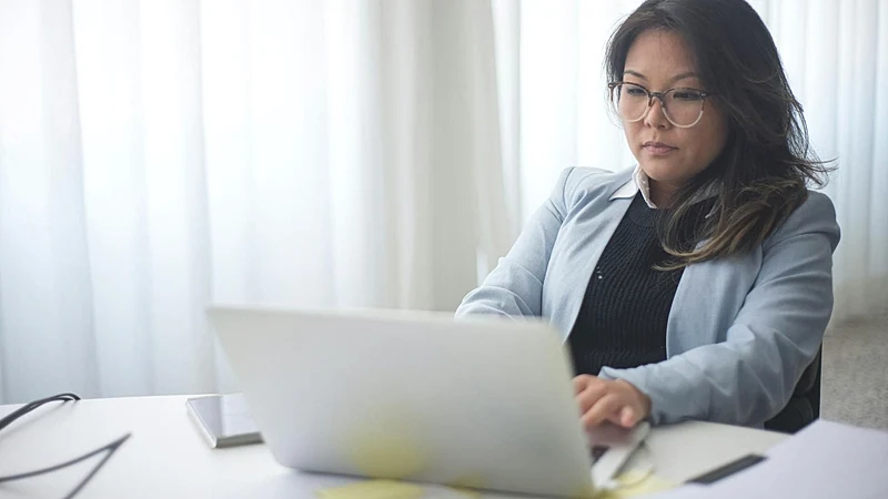 Focused businesswoman in office working on laptop with documents on the desk.