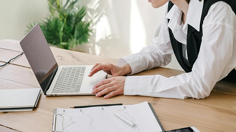 Professional woman using laptop at a wooden desk with office supplies.