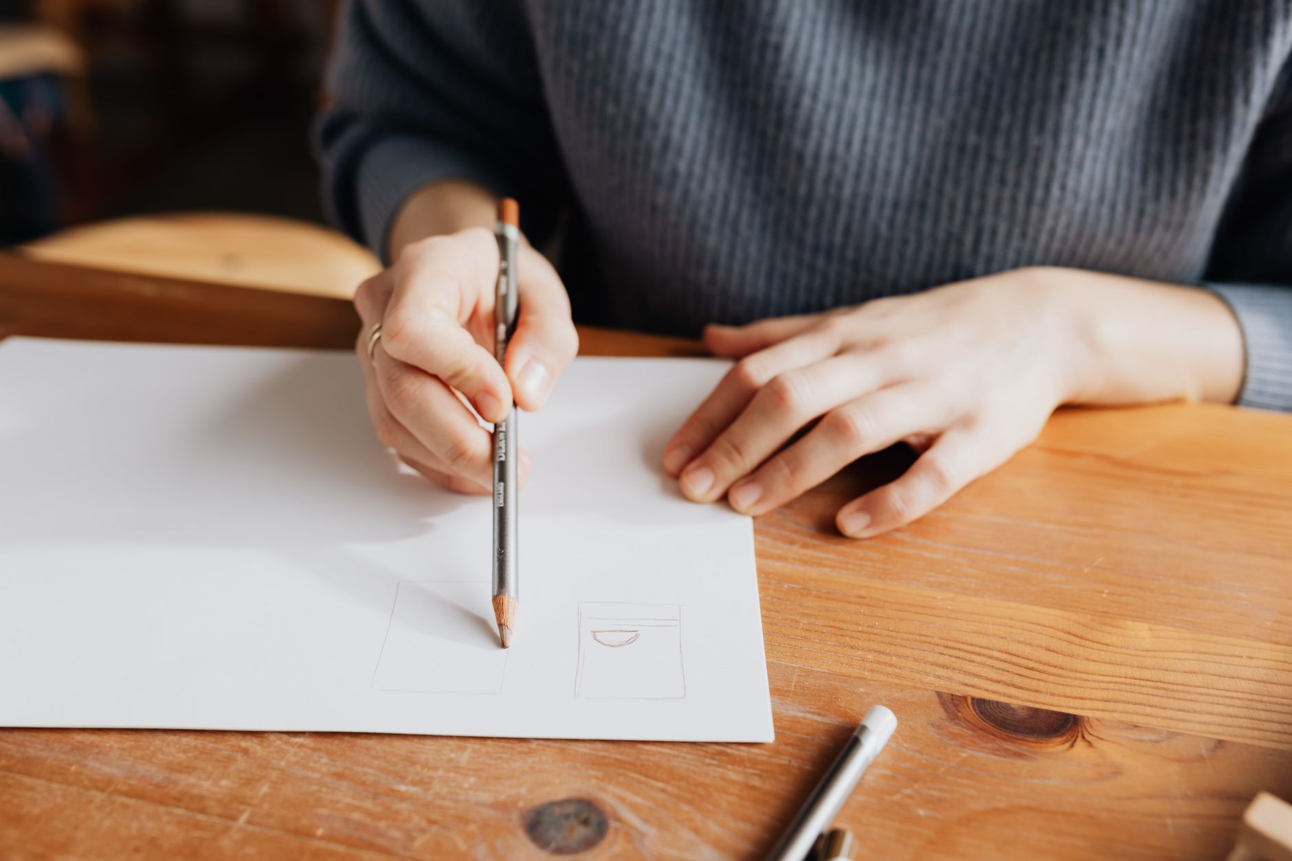 Person sketching on white paper with pencil on a wooden table, showcasing artistic creativity.