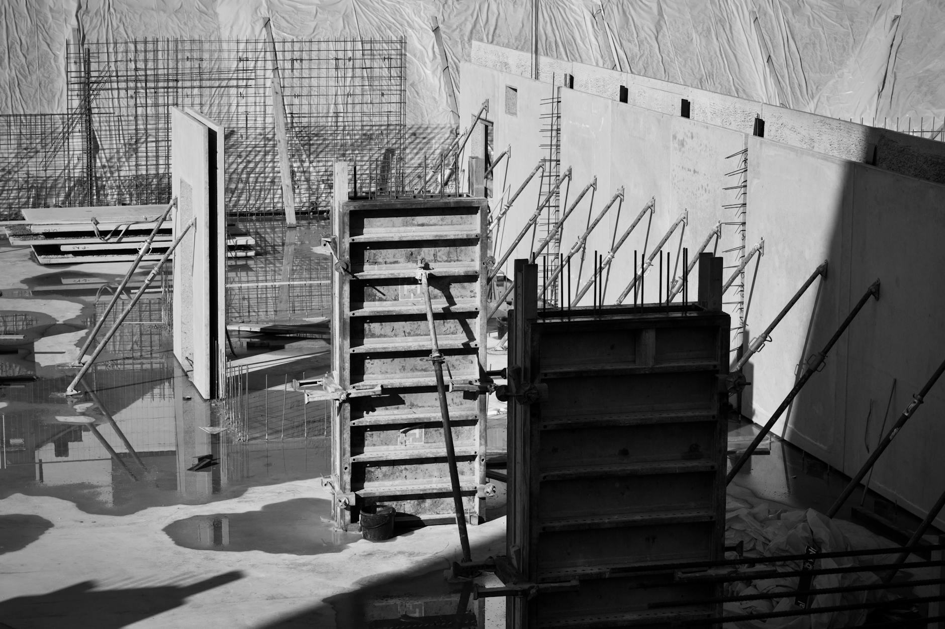 Monochrome view of a construction site with concrete forms and metal reinforcements.