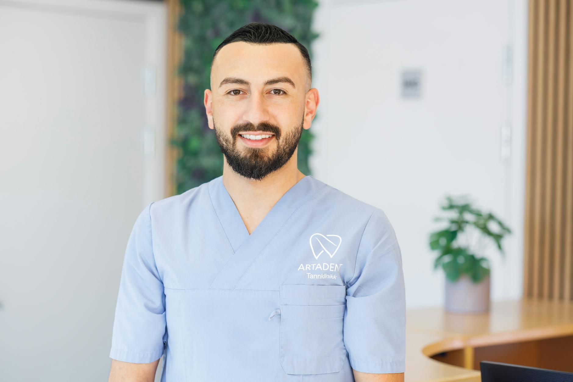 A friendly dentist in scrubs standing in a bright, modern dental office, ready to assist patients.