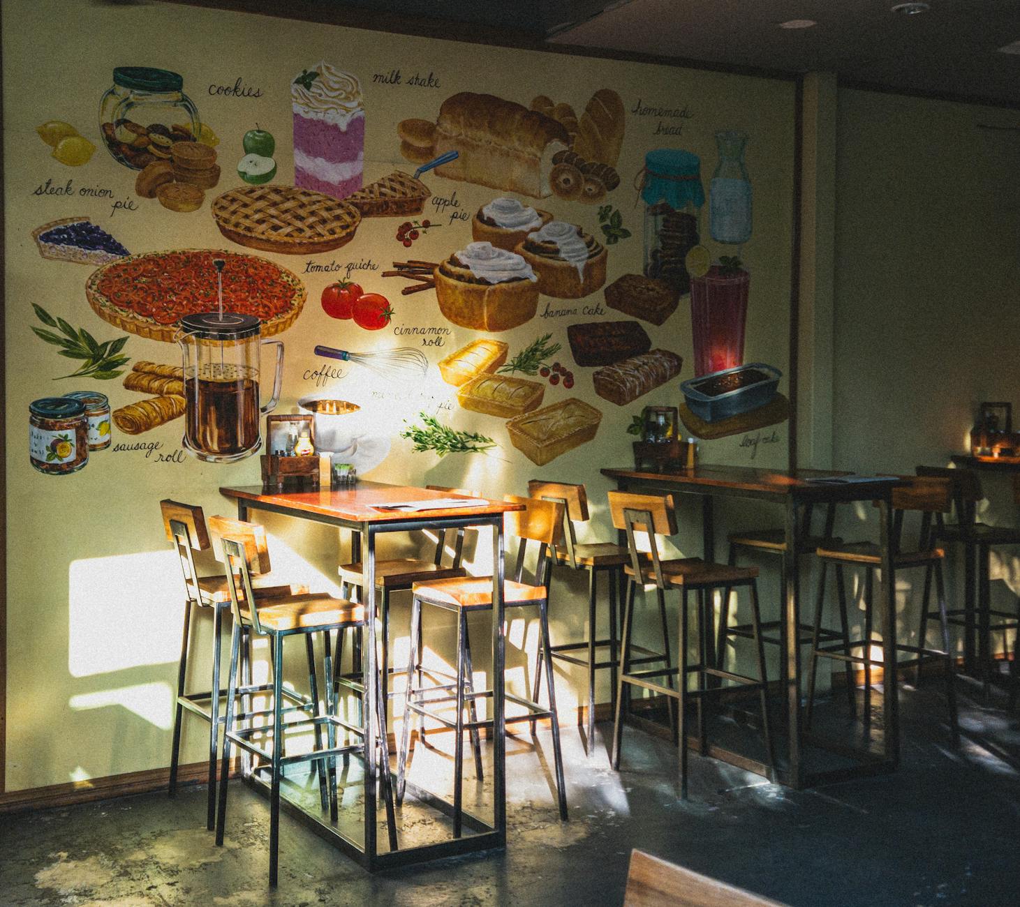 Warm sunlight illuminates a cozy café interior, showcasing vibrant wall art depicting various foods.