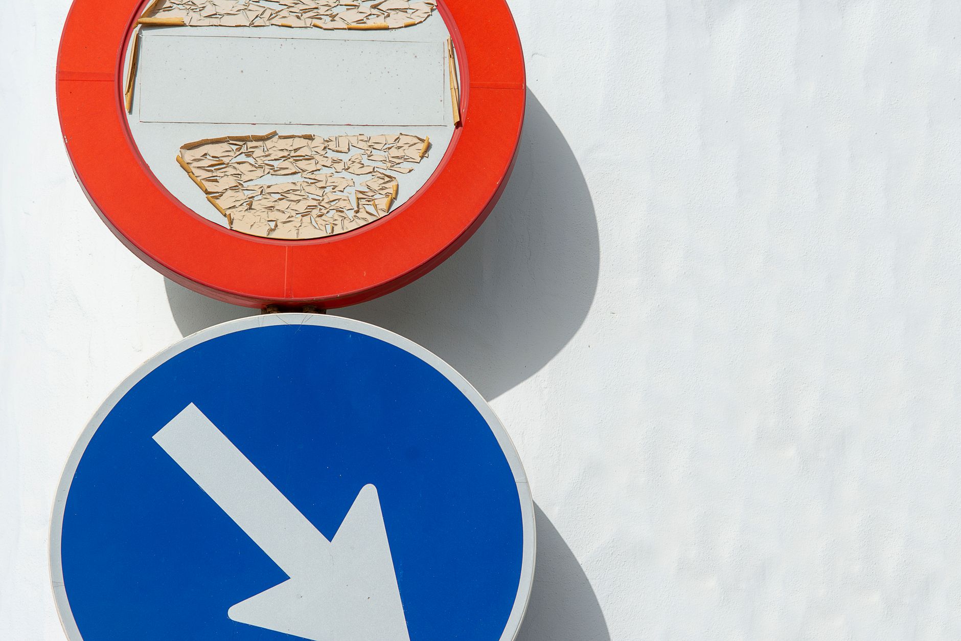Close view of aged traffic signs with peeling paint under bright sunlight.