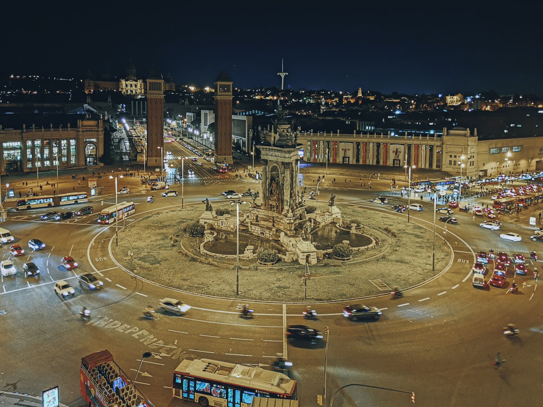 Illuminated Plaza de España roundabout in Barcelona with cars and city lights.