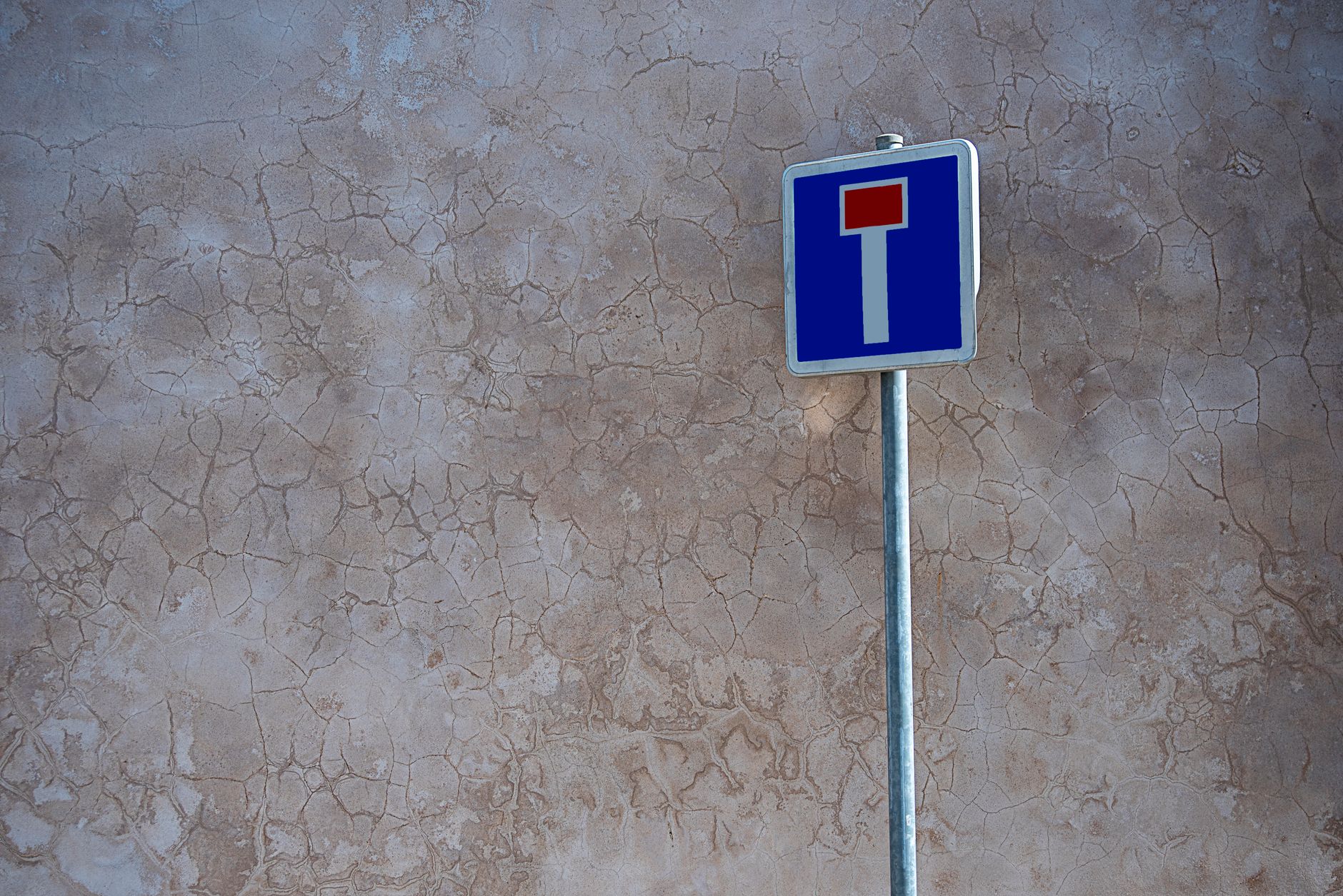 A dead end road sign against a cracked, textured concrete wall outdoors.