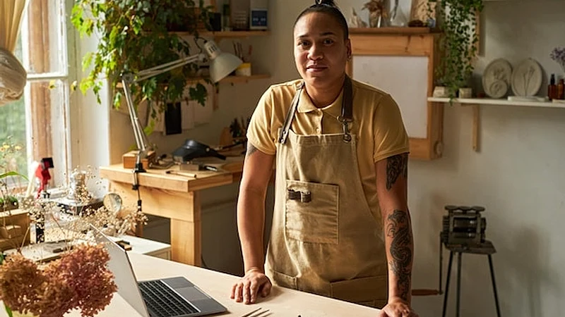 Waist up portrait of tattooed female artist looking at camera and smiling while standing in cozy stu