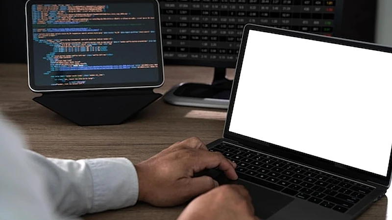 Close up of hands typing on a laptop at an office desk with a blank screen mockup and copy space programming code and data analysis setup in the background