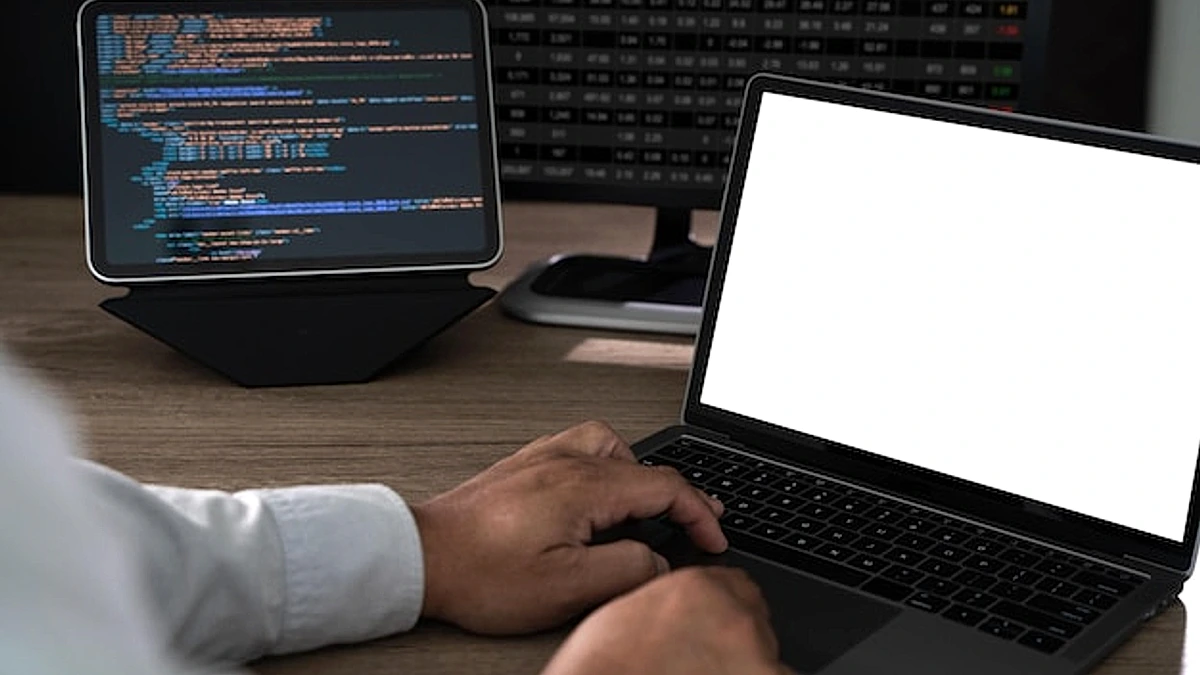 Close up of hands typing on a laptop at an office desk with a blank screen mockup and copy space programming code and data analysis setup in the background