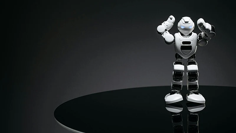 A small humanoid robot with glowing eyes on a reflective table in a dark setting.