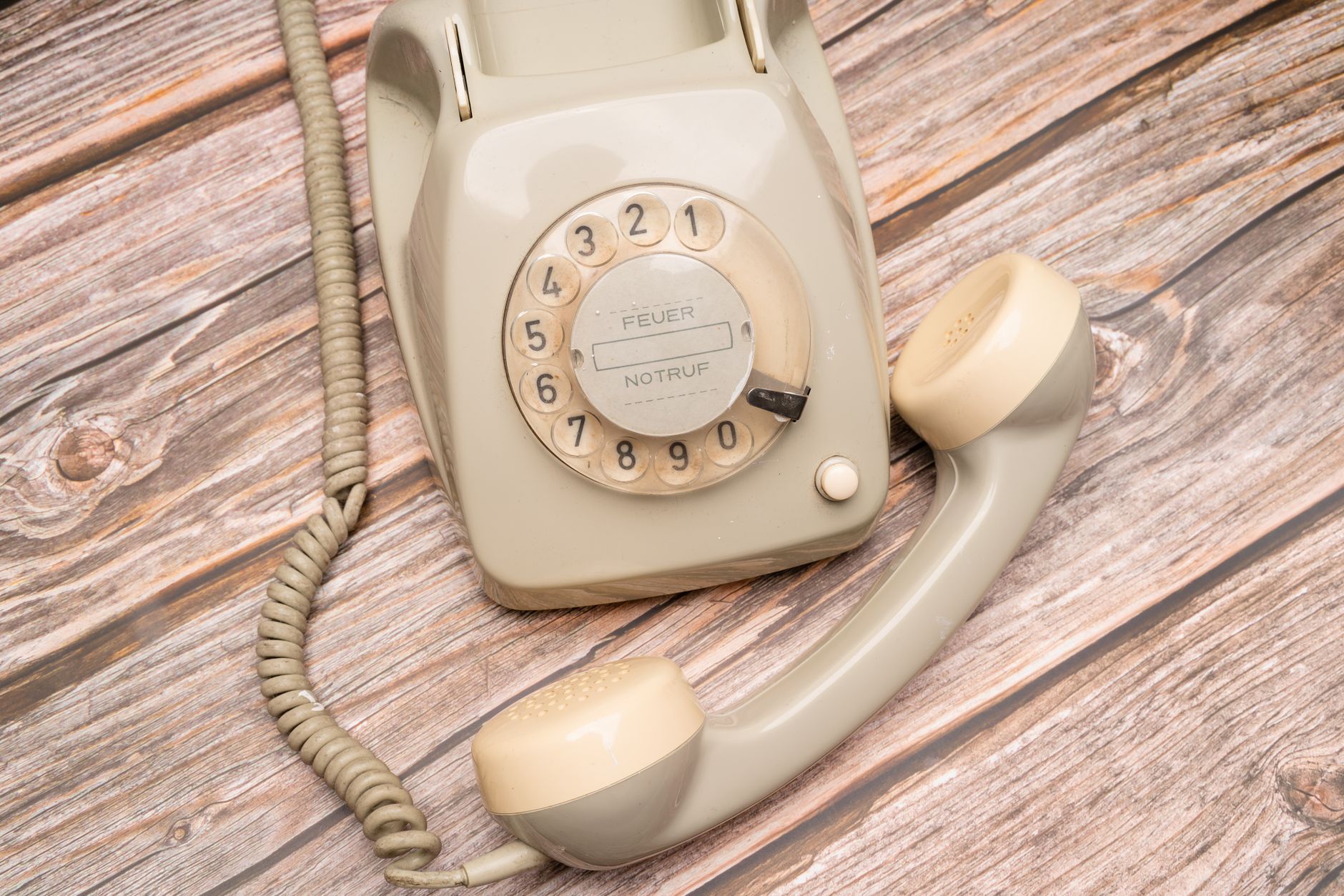 Classic beige rotary dial telephone on wooden surface with nostalgic feel.