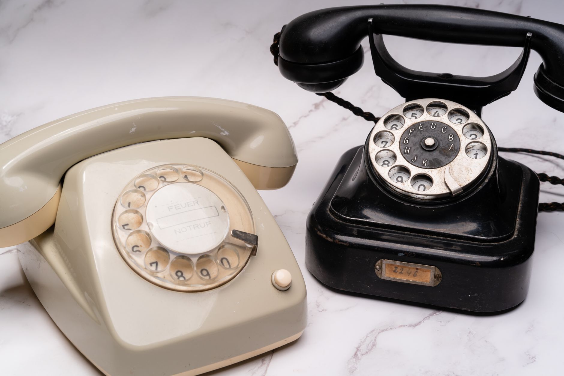Two classic rotary dial telephones, one black and one beige, on a marble surface.
