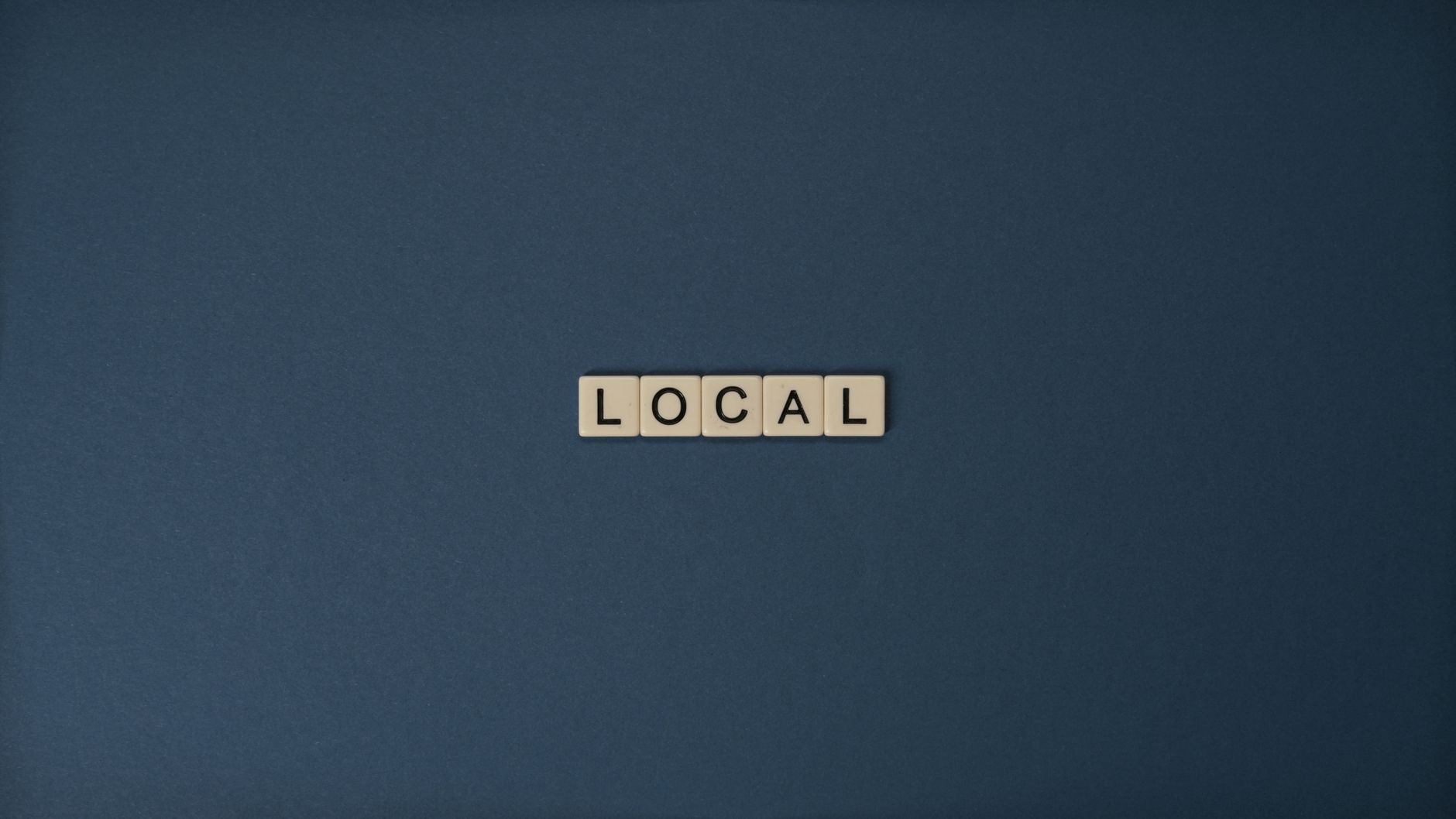 Flat lay of 'Local' in Scrabble tiles on a blue background, with ample copy space.
