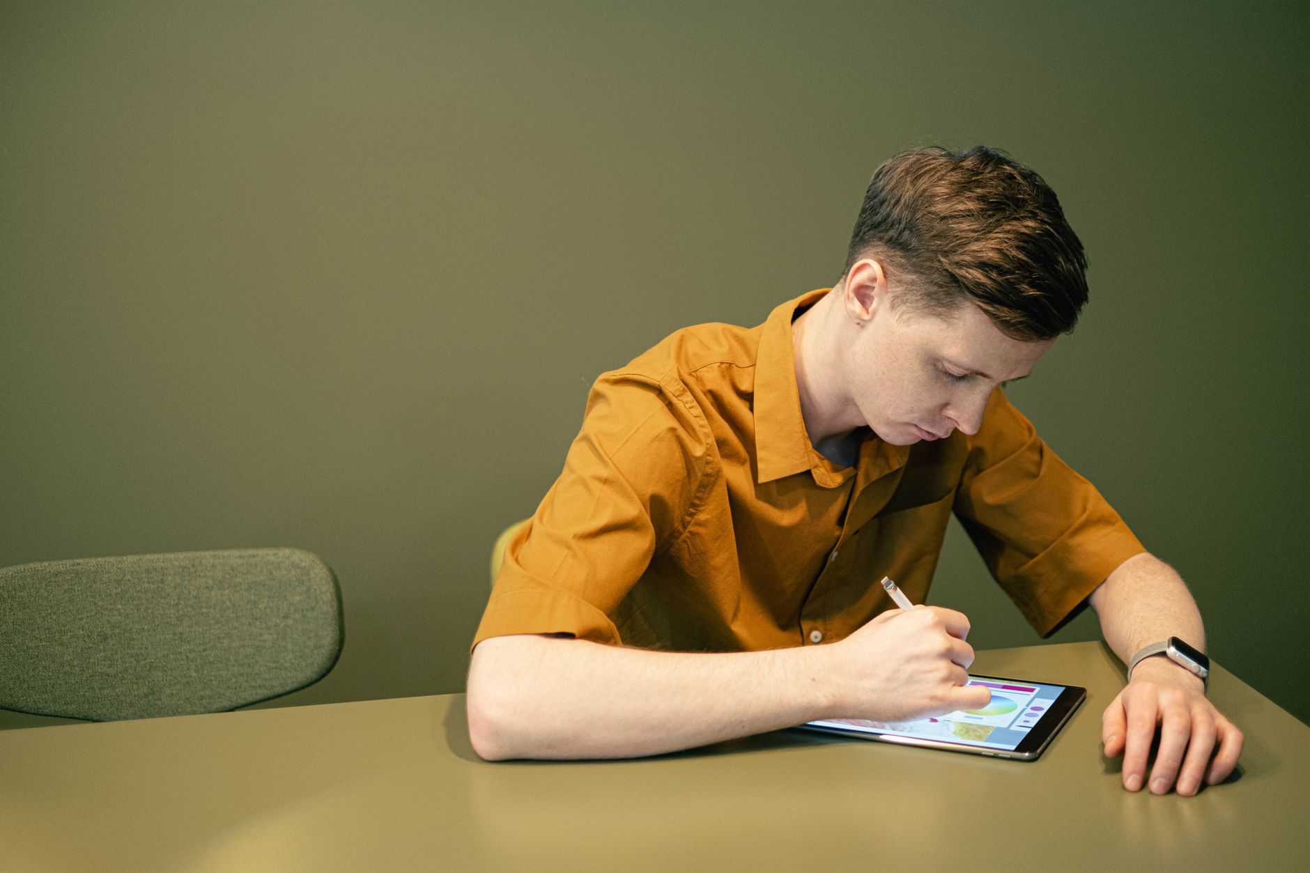 A young man sketches on a tablet in a minimalist indoor environment, focusing intently.
