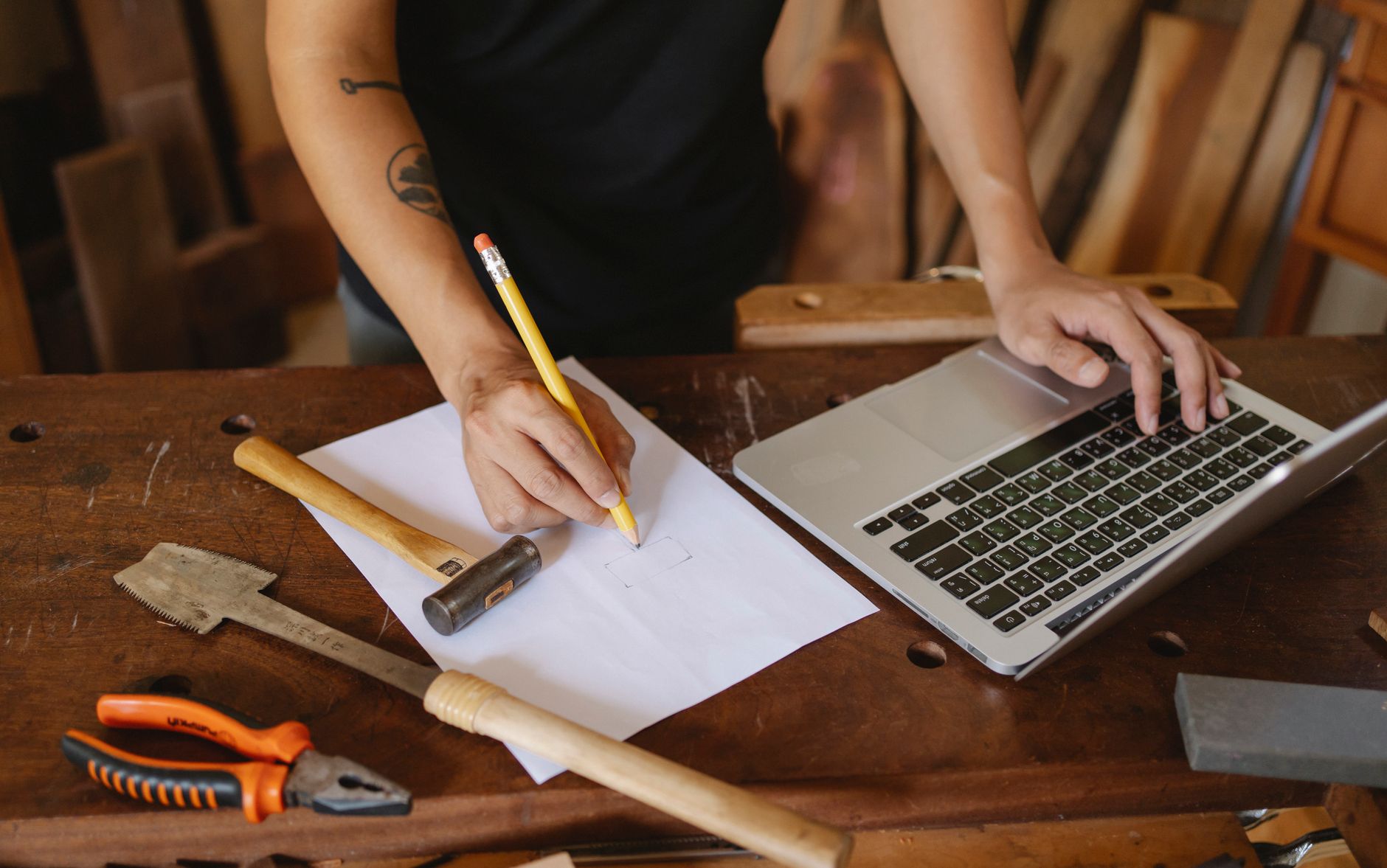 Crop faceless male worker standing near table and creating new craft Piece on paper while working with laptop