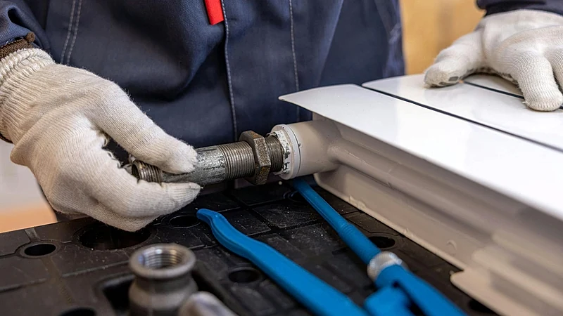Close-up of a plumber installing a radiator pipe using specialized tools.