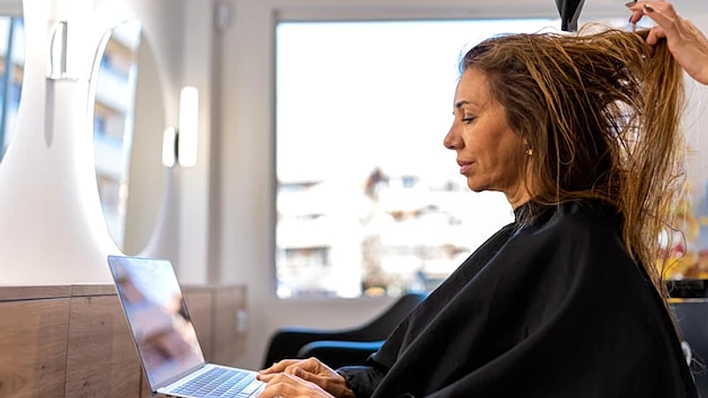 Woman working on laptop while sitting in hairdressing salon