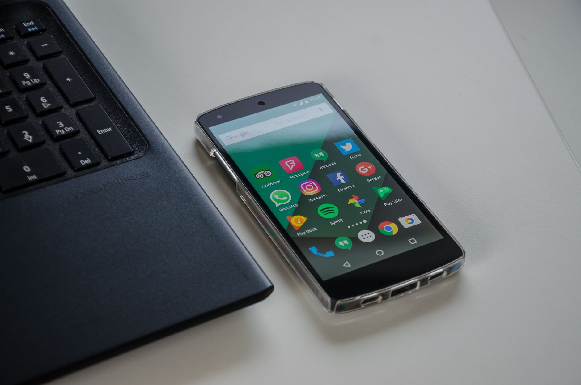 Smartphone on a table showing various social media apps beside a laptop keyboard.