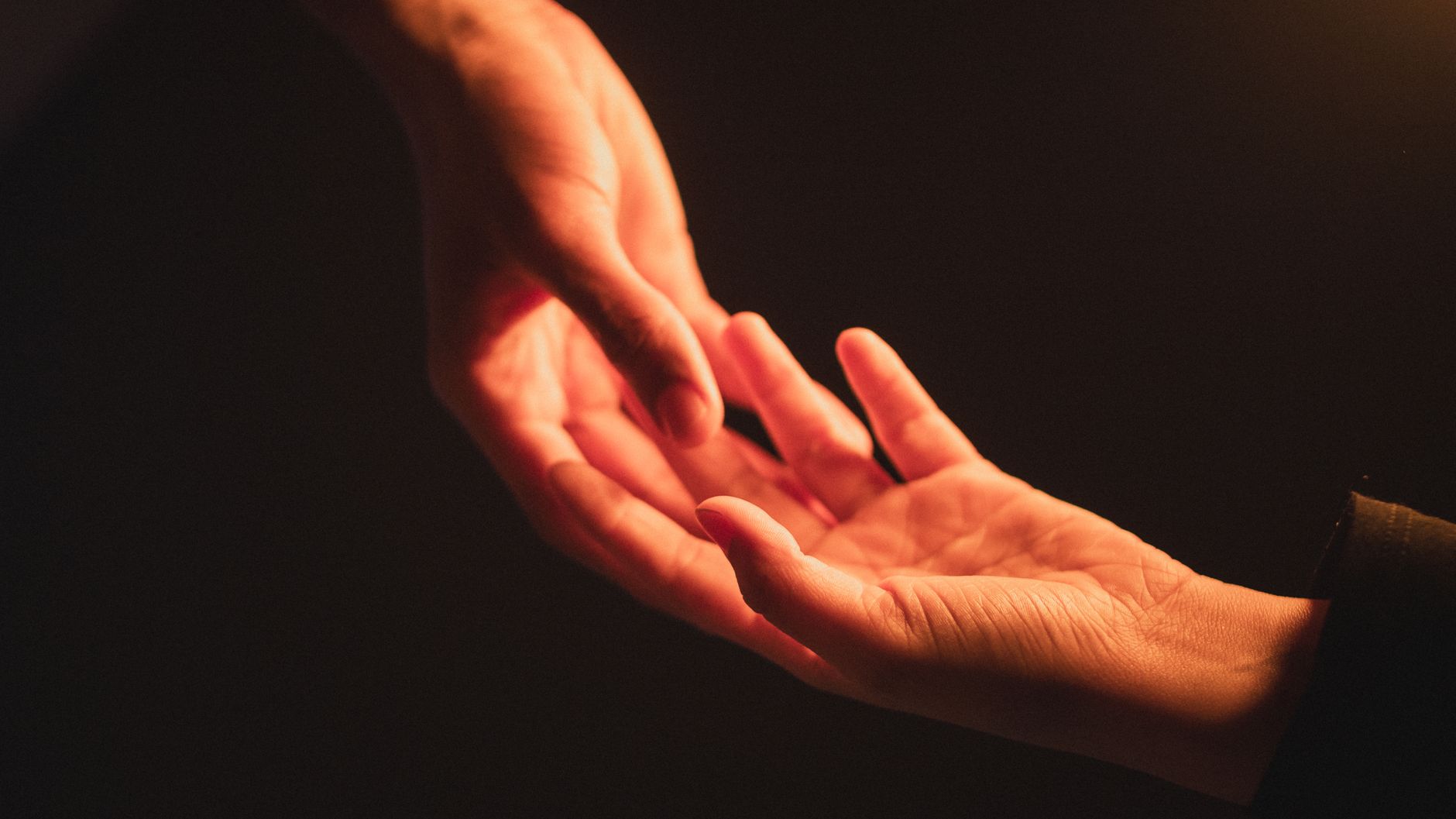 A warm and intimate close-up of hands reaching towards each other in dim light, symbolizing connection.