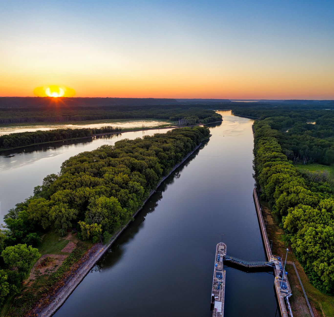 A drone captures a serene water canal surrounded by lush trees at sunset in Welch, Minnesota.