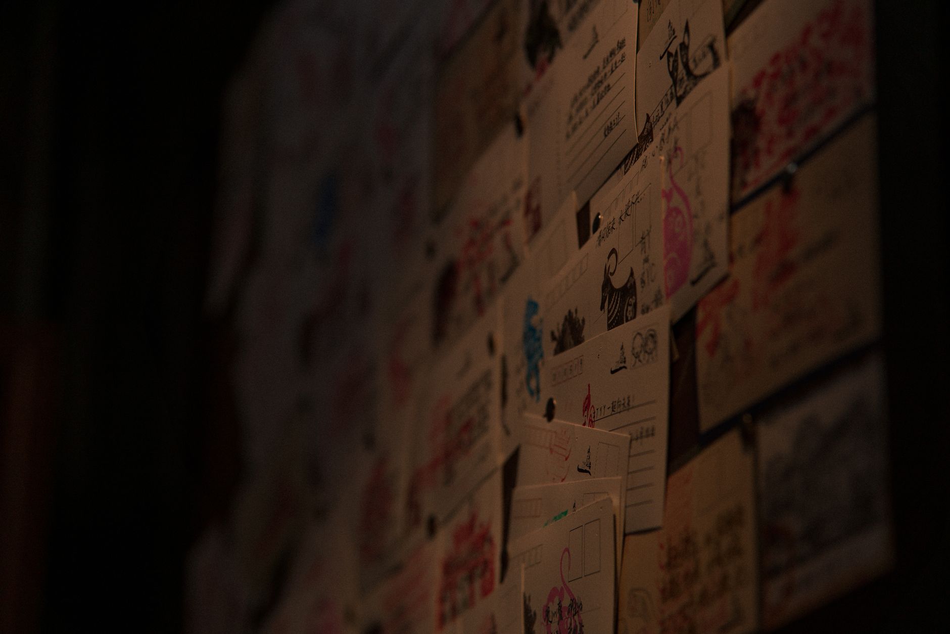 A creative display of diverse postcards and illustrations adorns a dimly lit wall.